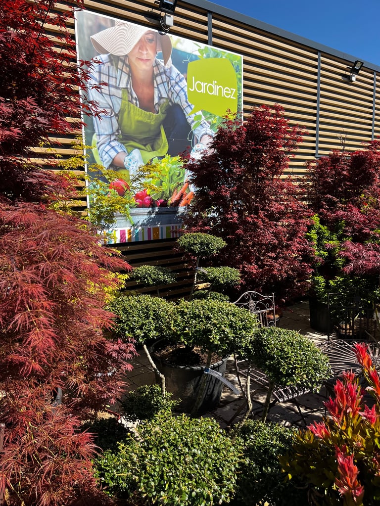 Écran de jardinerie avec banderole souriant jardinier entouré de lierre vibrant et plantes fleuries contre une façade en bois moderne à lattes
